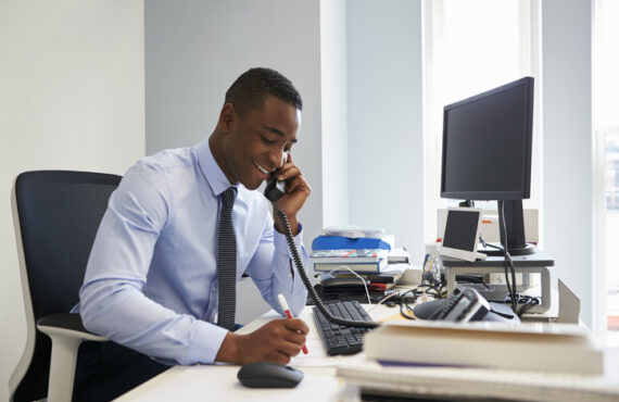 Young black businessman using the phone at his office desk